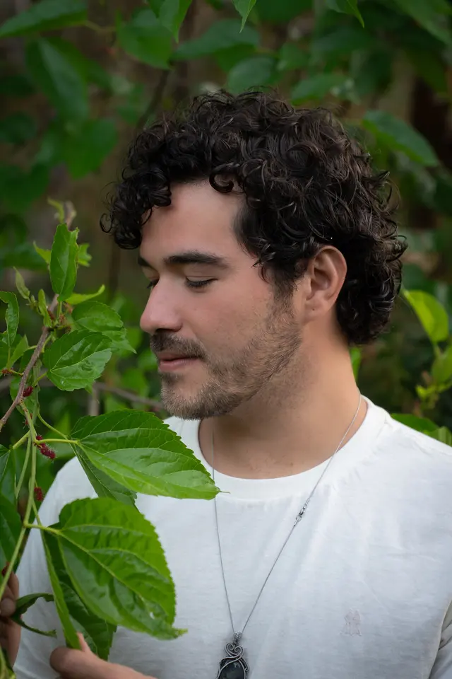 Fellipe Oliveira, terapeuta de ThetaHealing®, de perfil entre folhas